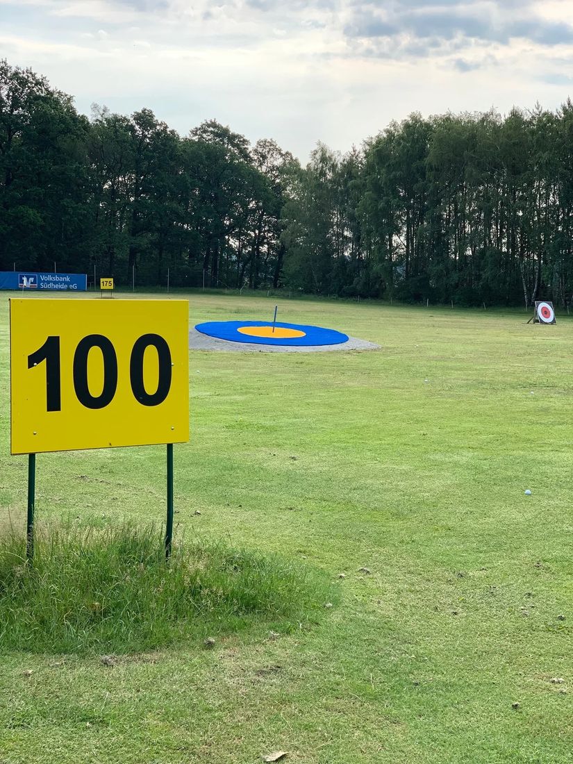 Driving Range mit 100-Meter-Marke, blau-orangefarbenem Zielgrün und Waldrand im Hintergrund